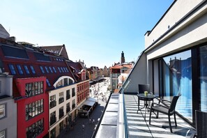 A narrow street with buildings on either side, a clear sky, and a balcony with outdoor seating. - DUKES Apartments - Old Town (Wroclaw)