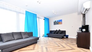 A modern living room with a grey sofa, a second grey sofa, a herringbone wooden floor, a coffee machine, and a wall-mounted air conditioner. - DUKES Apartments - Old Town (Wroclaw)
