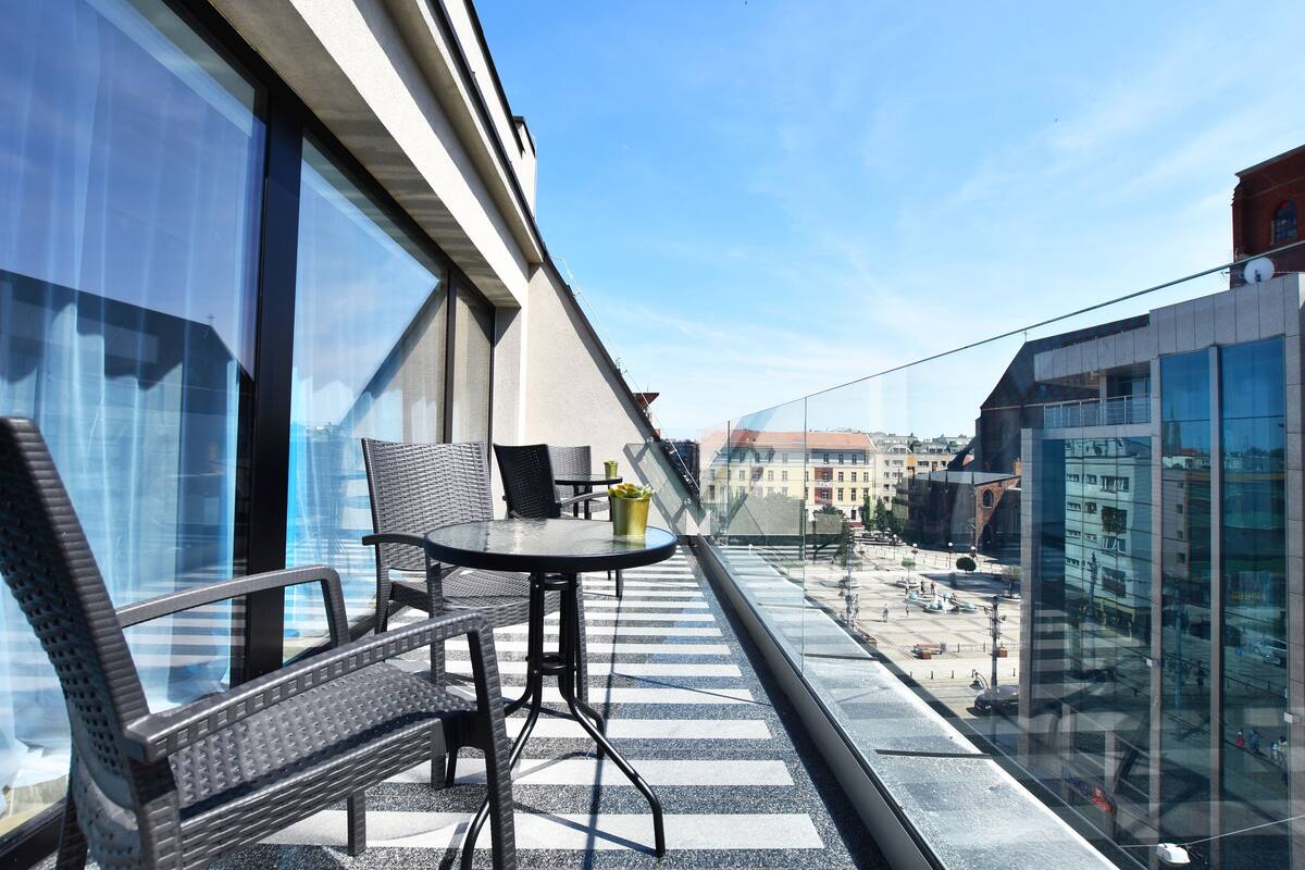 A balcony with a table and chairs, large windows, and a view of the cityscape.