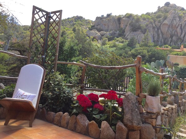 A patio with a lounge chair, a wooden trellis, and a stone wall.