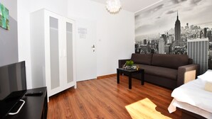Ett modernt rum med trägolv, en svart soffa, en vit garderob, ett svart soffbord och en väggmålning som föreställer en stadsbild.