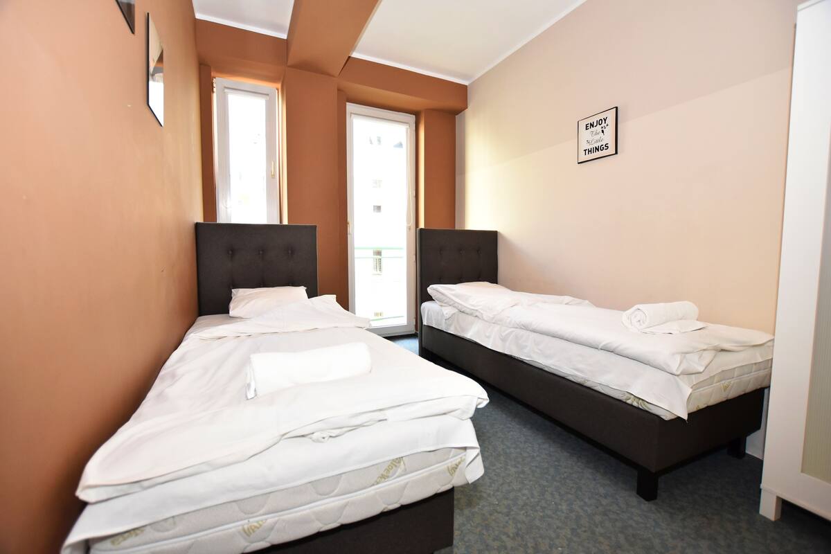 A hotel room with two single beds, a door, and a window.