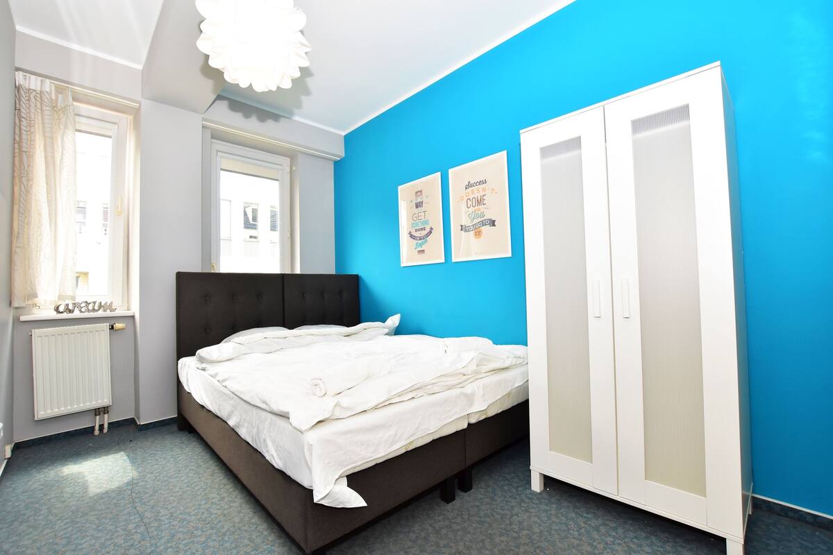 A bedroom with a bed, a wardrobe, a radiator, and two wall art pieces.