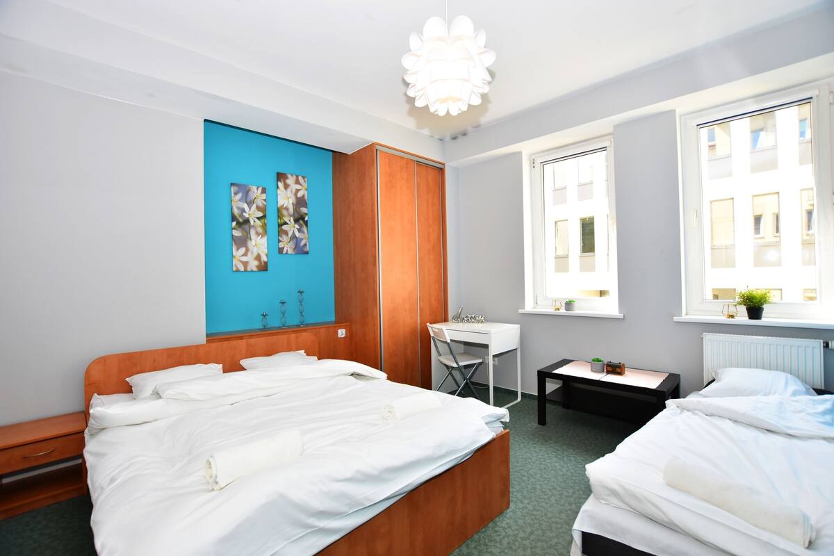 A hotel room with a large bed, a desk, a chair, and a window with a view of buildings.