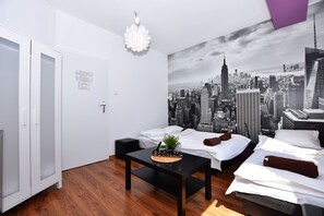 Habitación de hotel con dos camas, un mural de paisaje urbano, una mesita con una planta y una puerta blanca.