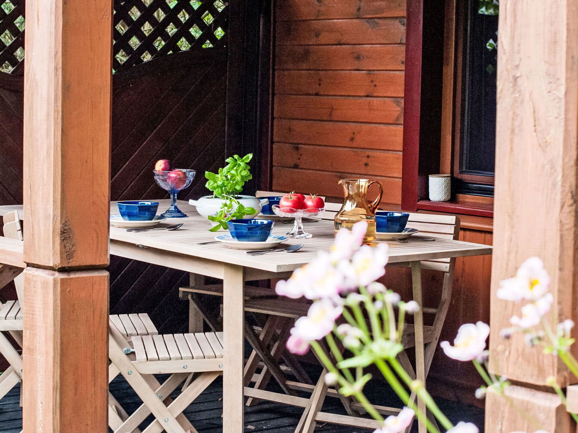 An outdoor dining area with a wooden table set for two, surrounded by wooden chairs.