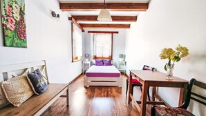 Una habitación acogedora con una cama de madera, un banco de madera, una mesita y un florero con flores.