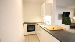 Eine kleine Küche mit weißen Schränken, einem schwarzen Backofen, einer Holz Schneidebrett und einem Spülbecken.