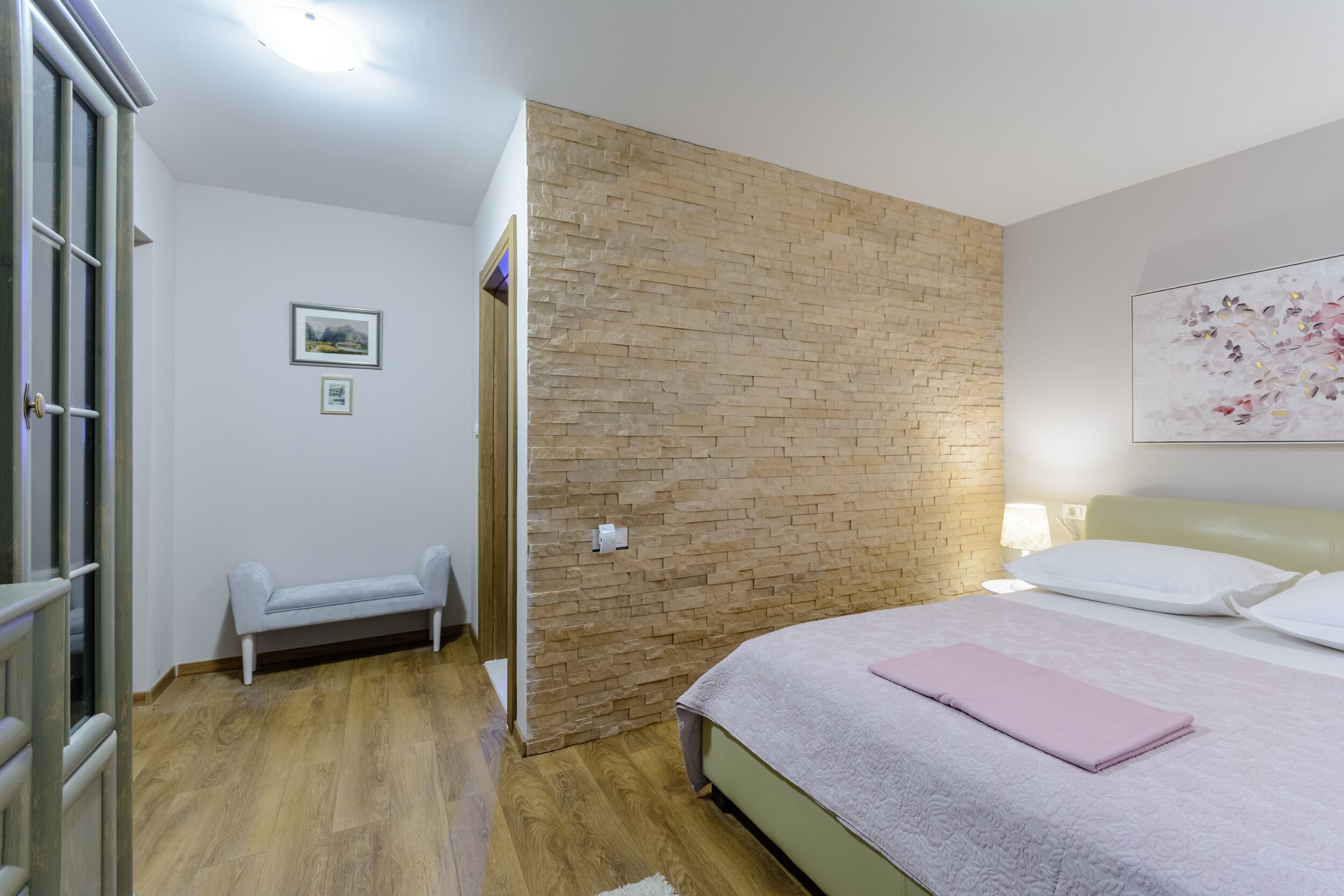 Une chambre avec un lit, un banc, un mur décoratif en briques et un tableau.