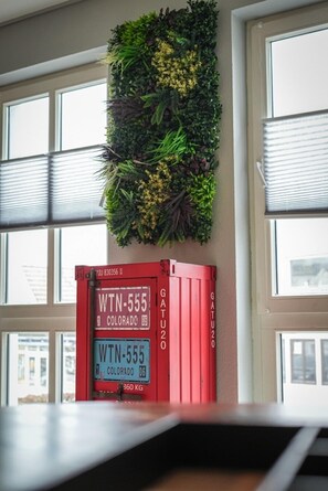 A wall-mounted vertical garden with a red shipping container labeled 'WTN-555 COLORADO 06' and '360 KG' in front of a window.