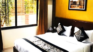 Una camera d'albergo con un letto grande, un climatizzatore, una ventola a soffitto, una finestra con tende e un quadro appeso al muro.