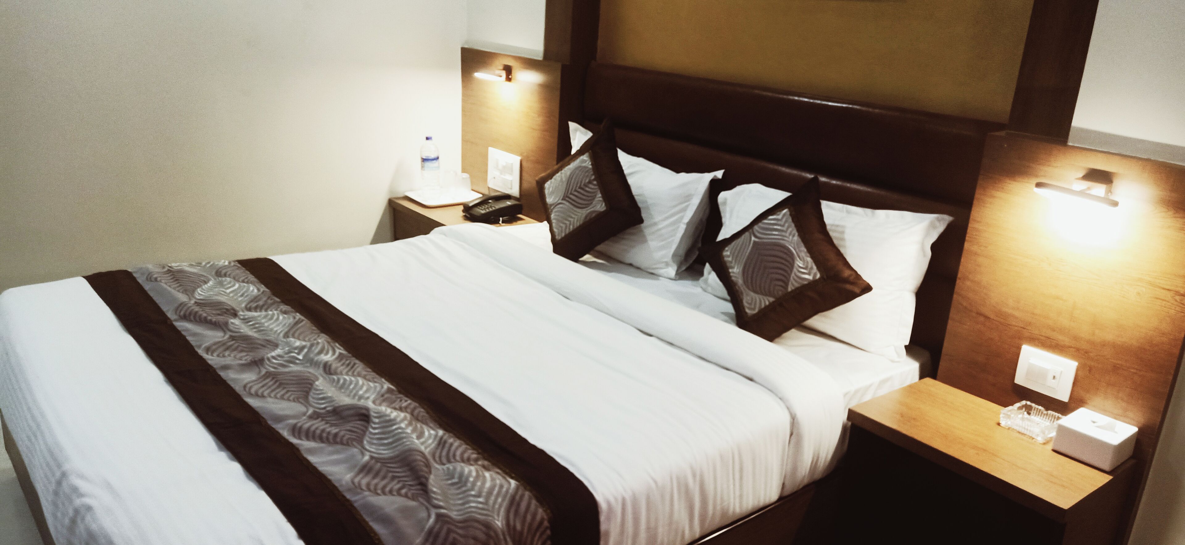 A neatly made bed with white and brown bedding, two bedside tables with lamps, and a wooden headboard.