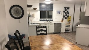 Une cuisine avec des meubles blancs, une table à manger en bois et une horloge noire accrochée au mur.