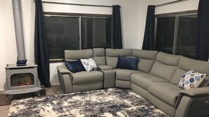 Un salon comprenant un canapé d’angle, une cheminée et une grande fenêtre avec des rideaux.