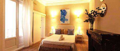 Una habitación de hotel con una cama, una chimenea, un cuadro y dos apliques de pared.