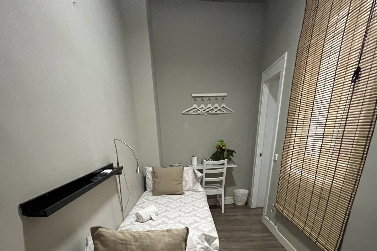 A narrow hallway with two beds, a desk, and a hanging light fixture.
