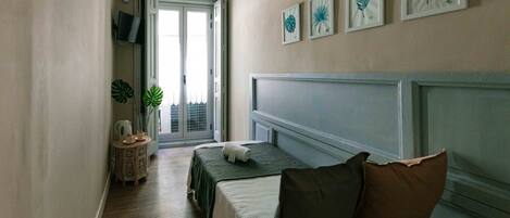 A hotel room with a bed, a small table with a plant, and framed artwork on the wall.