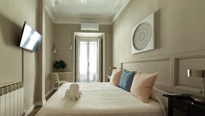 A hotel room with a large bed, a flat-screen TV, a decorative wall piece, and a view of the city through the door. - El HostALL (Madrid)