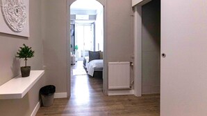 A hallway with a white door, a radiator, a plant, and a trash bin. - El HostALL (Madrid)