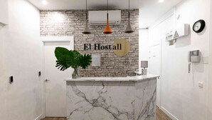 A reception desk with a marble top, a sign reading "El Hostal", and a plant on the counter. - El HostALL (Madrid)