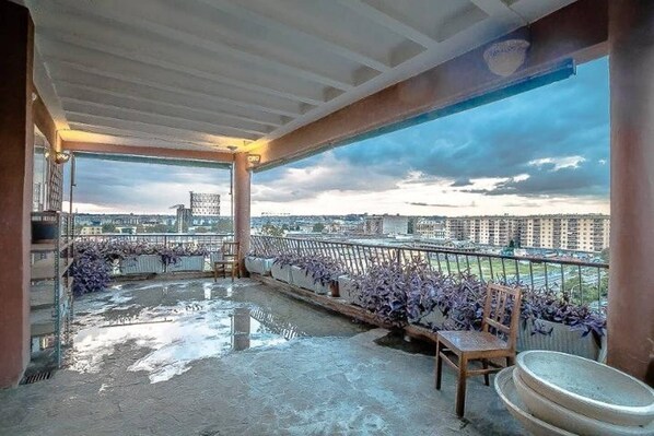 Enjoy the city view from this balcony with a chair, table, and potted plants.