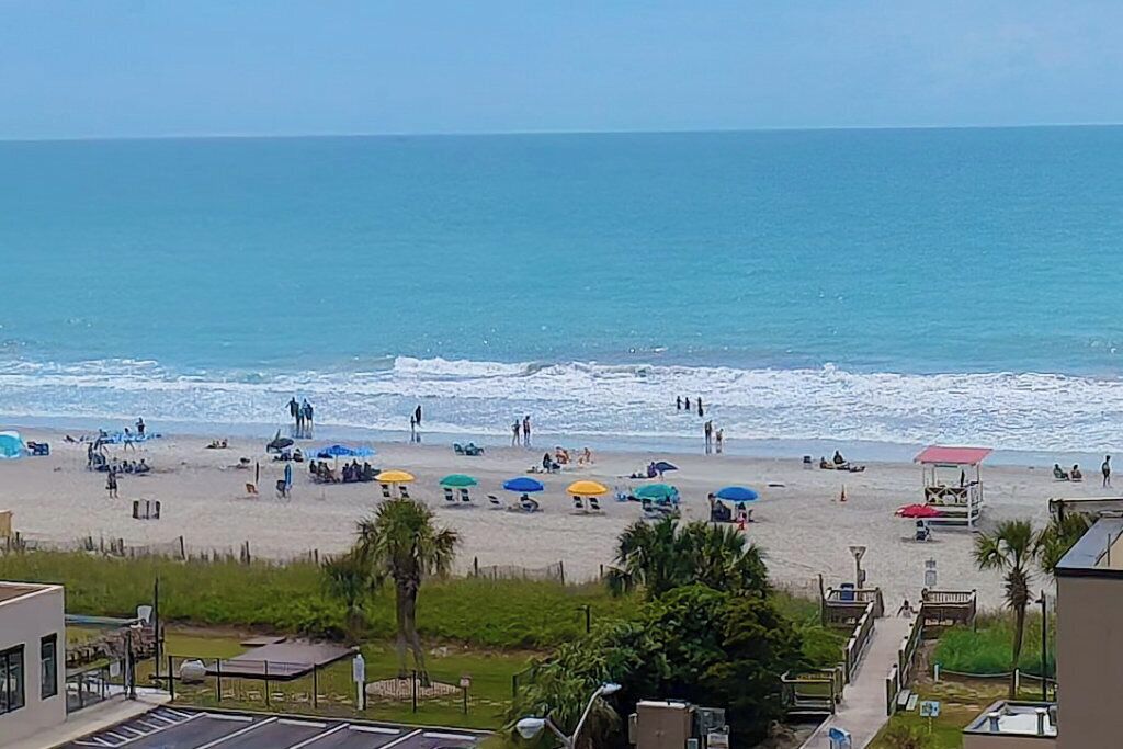 Una spiaggia con ombrelloni, una torretta di salvataggio e una vista limpida sull'oceano.