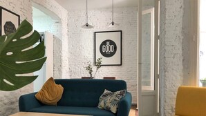 Ein modernes Wohnzimmer mit einem blauen Sofa, einem gelben Sessel und einem Couchtisch aus Holz. Eine große Grünpflanze, ein gerahmtes inspirierendes Zitat an der Wand und ein Fenster, das für natürliches Licht sorgt.