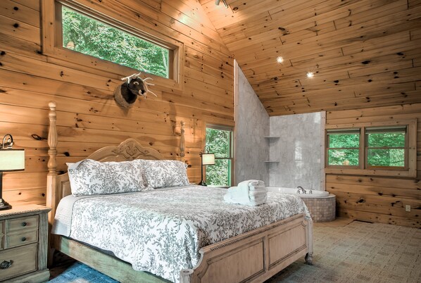 A wooden cabin bedroom with a bed, nightstands, a lamp, a decorative animal head, and a shower area.