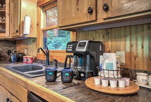 A kitchen with wooden cabinets, a coffee maker, mugs, and a coffee machine.