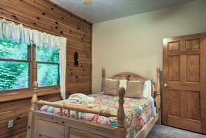 Ein Zimmer mit Holzwandverkleidung, einem Bett, einem Fenster mit Vorhängen und einer Tür.