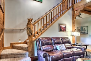 A wooden staircase with a bear sculpture at the top, a leather sofa with a cushion, and a framed picture on the wall.