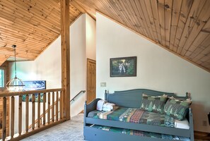 Ein Schlafzimmer mit schrägem Dach, einem Bett mit gemusterten Betttextilien, einem Bild an der Wand und einem Holzbalken.