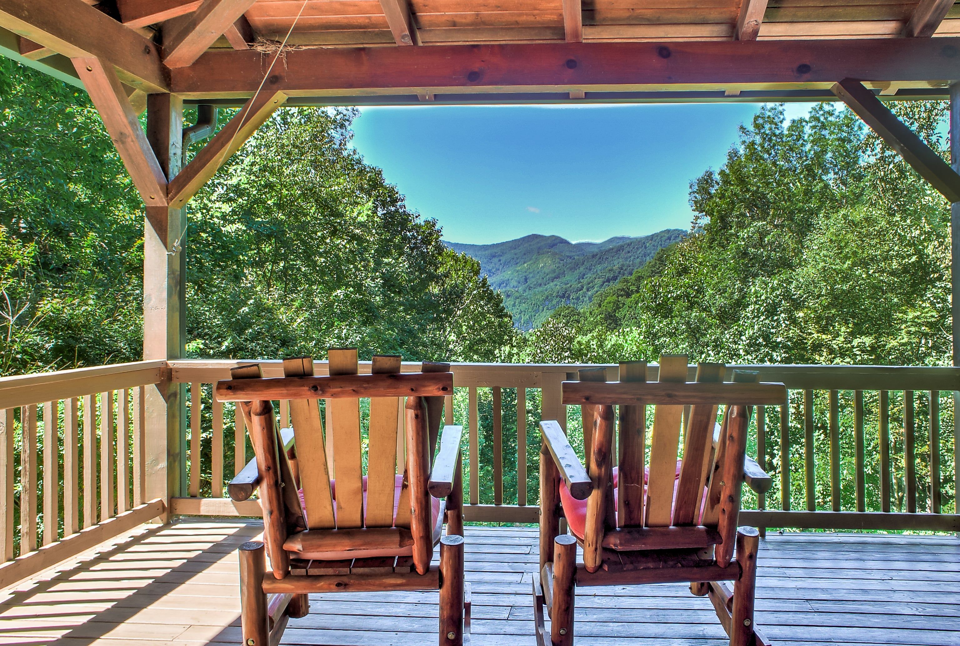 A wooden deck with two rocking chairs facing a mountainous landscape.