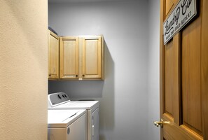 A laundry room with a washing machine, wooden cabinets, and a door with a sign indicating the room's purpose.