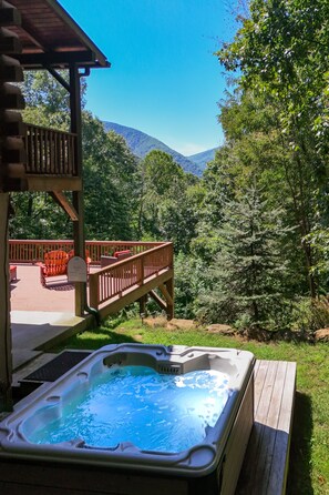 A hot tub on a wooden deck with a view of a mountain and forest.