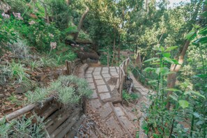 A stone pathway leading through a forested area with a wooden fence on one side.