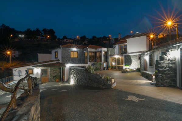 A well-lit residential area with stone buildings, a paved driveway, and a wooden fence.