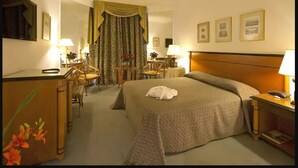 Een hotelkamer met een groot bed, een bureau met stoel, een klein tafeltje met lamp en een spiegel.
