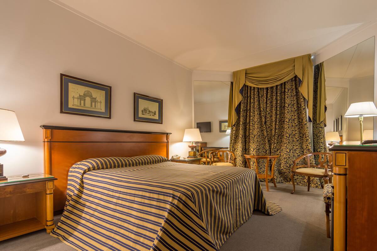 Een hotelkamer met een groot bed, twee nachtkastjes met lampen, een stoel, een bureau en een spiegel.