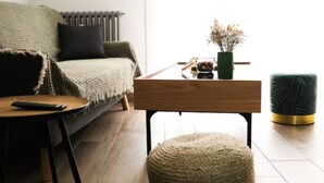 A cozy living room with a green sofa, a wooden side table, a small ottoman, and a radiator. - ★★ Le Grand Chambord ★★ (Laval)