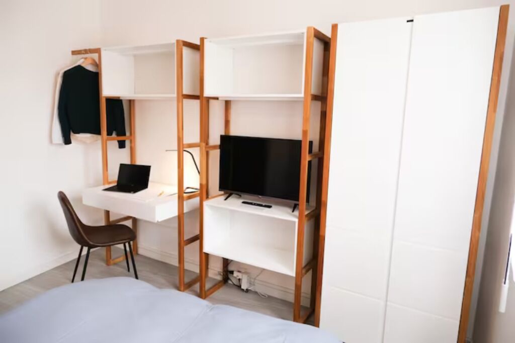 Ein Schlafzimmer mit Bett, Schreibtisch mit Laptop, Fernseher auf einem Regal und einem Kleiderschrank.