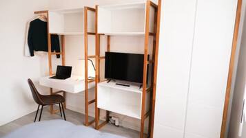 Ein Schlafzimmer mit Bett, Schreibtisch mit Laptop, Fernseher auf einem Regal und einem Kleiderschrank.