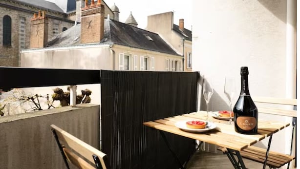 A balcony with a table set for two, a bottle of wine, and a view of historic buildings. - ★★ Le Grand Chambord ★★ (Laval)