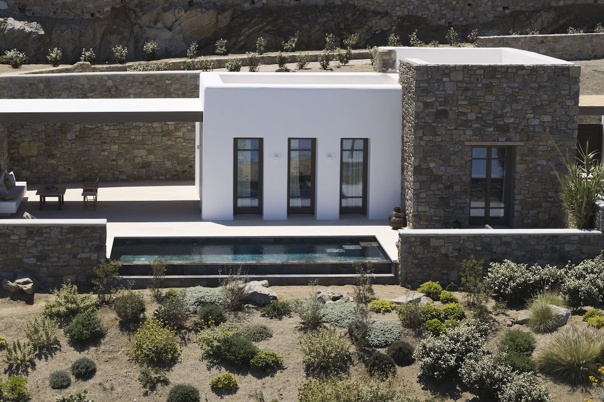 A modern house with a pool, stone walls, and a patio with outdoor furniture.