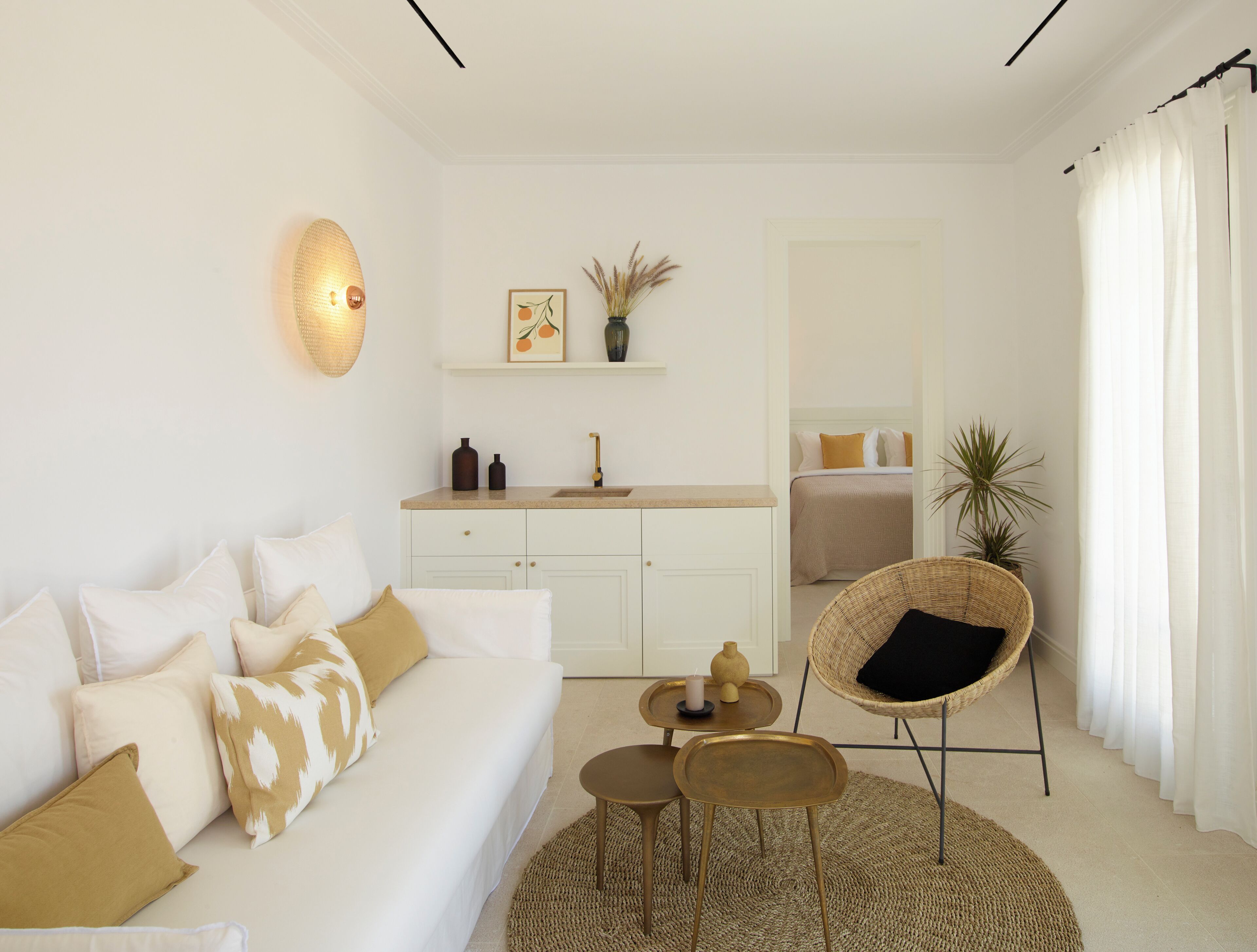 Een moderne woonkamer met een bank, salontafel en stoel, een keuken met een spoelbak en kasten, en een slaapkamer met een bed en gordijnen.