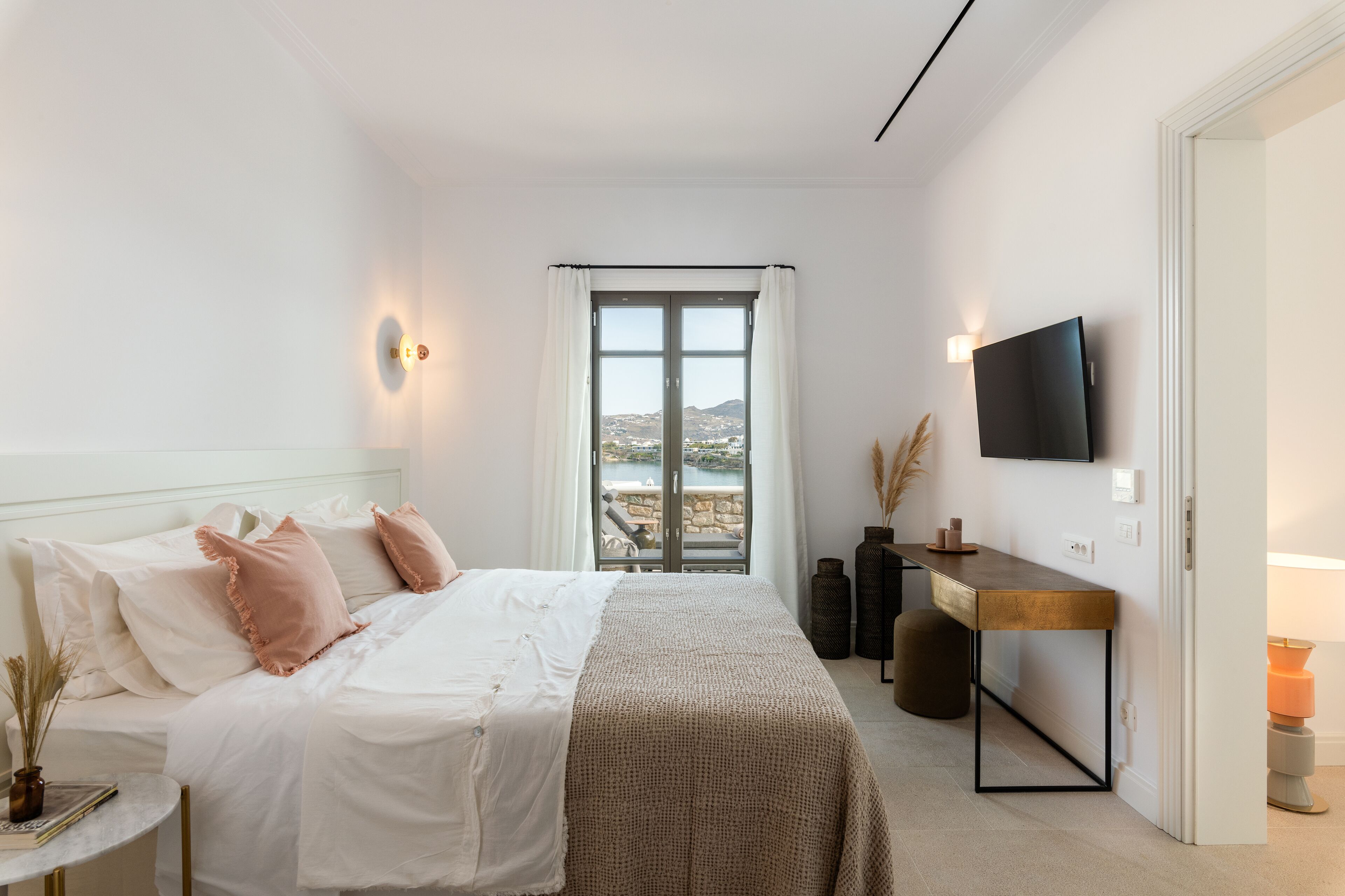 Ein Schlafzimmer mit Bett, Nachttisch, Lampe, Fernseher und Blick ins Freie.
