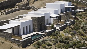 Et moderne feriested med flere bygninger med hvide tage, en swimmingpool og et stykke klippelandskab.