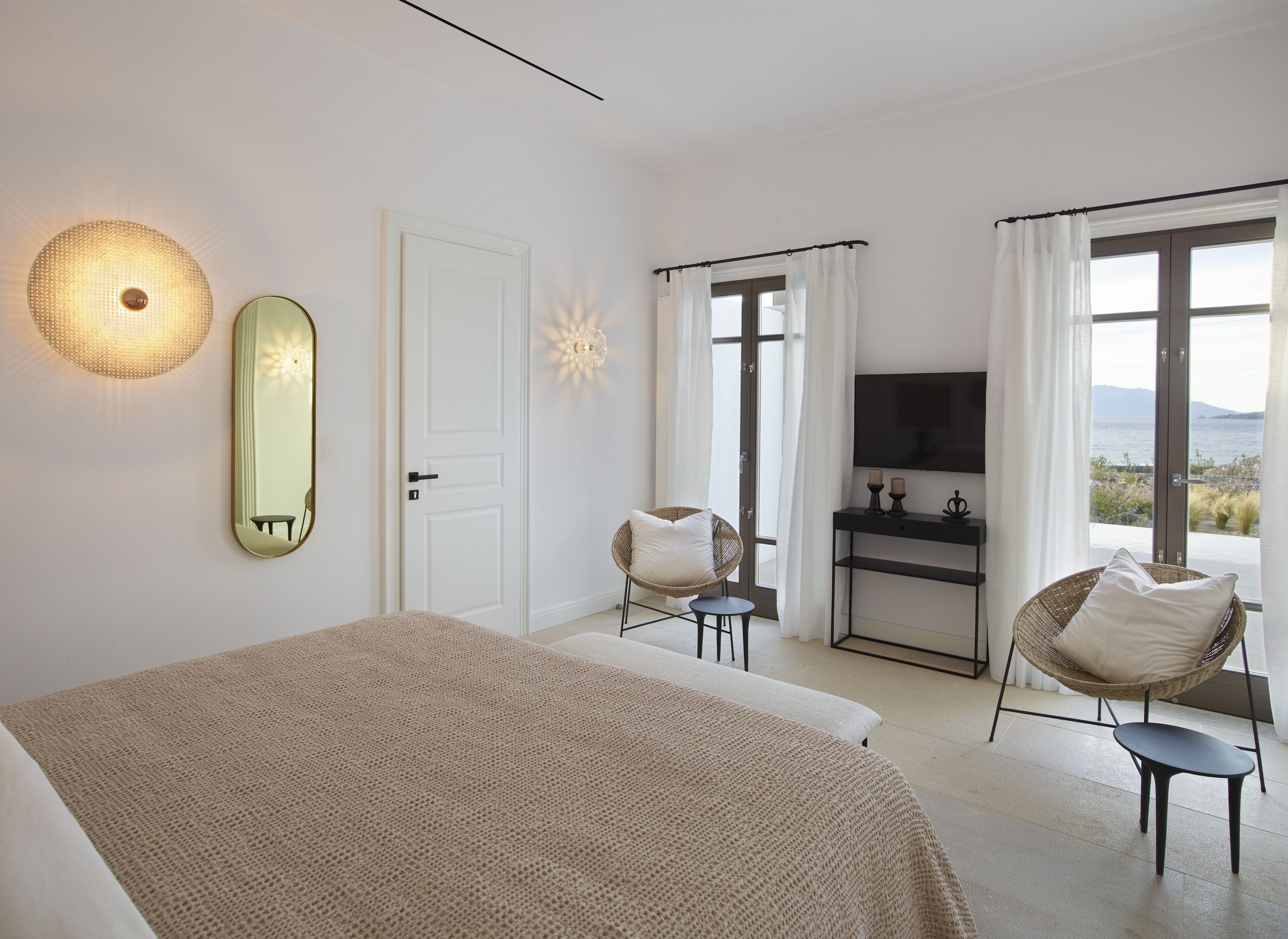 Un dormitorio con cama, una silla, un televisor y vista al mar.