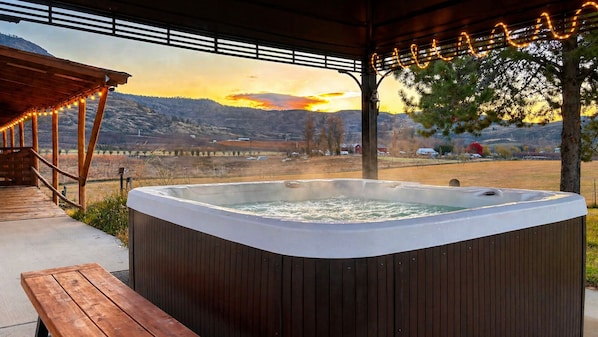 A hot tub in a covered outdoor area with a wooden bench and a view of a mountainous landscape.