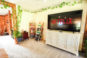 A cozy room with a large TV screen displaying 'NETFLIX,' a wooden log wall, a bookshelf, and a potted plant.